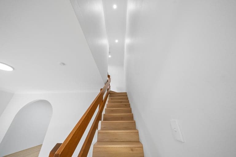 Oak stairwell rising between white walls and a timber handrail in Sydney
