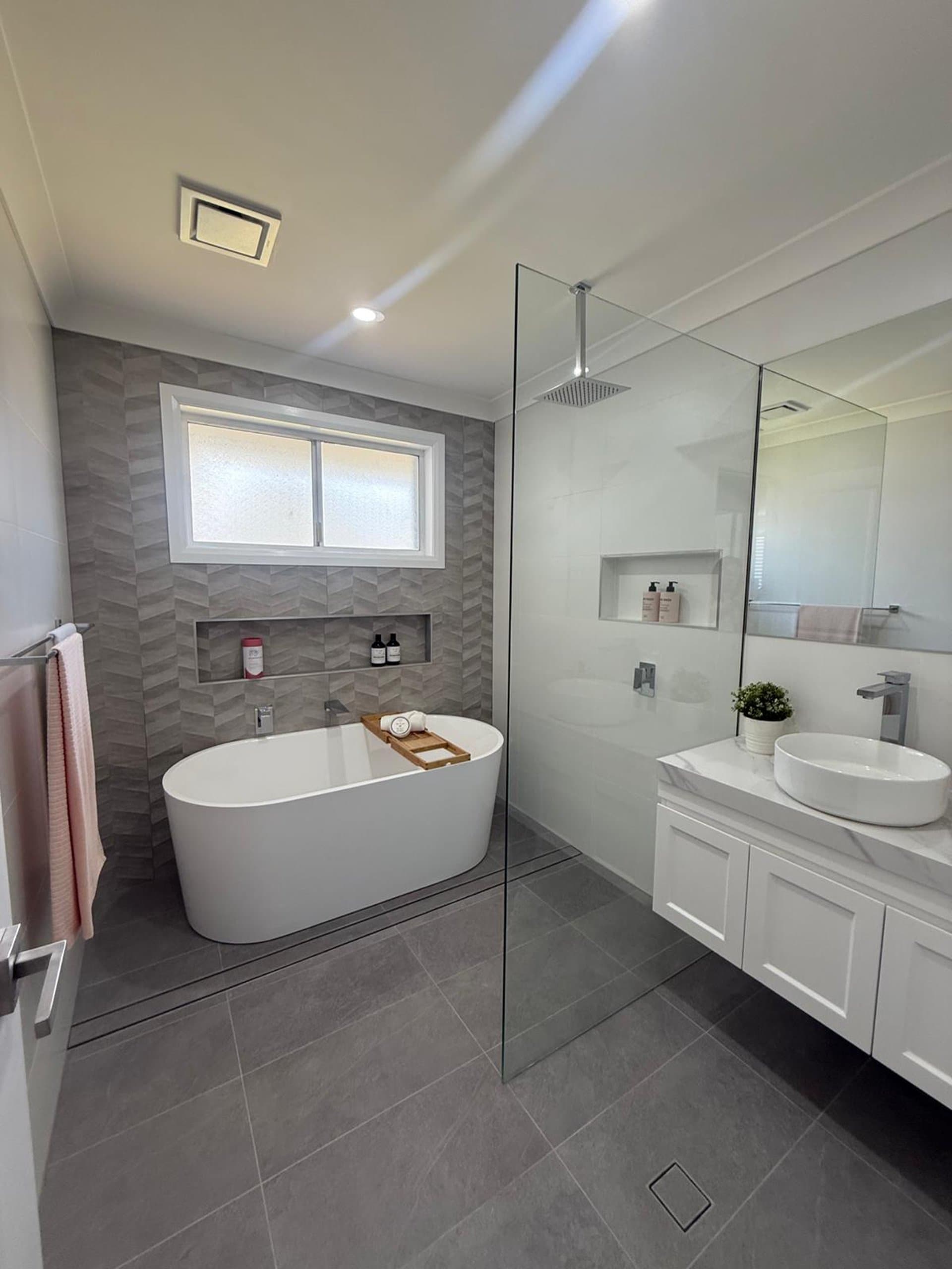 Grey tiled Sydney bathroom with a freestanding bath and glass shower