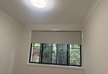 White roller blind fitted to a black-framed bedroom window in Sydney