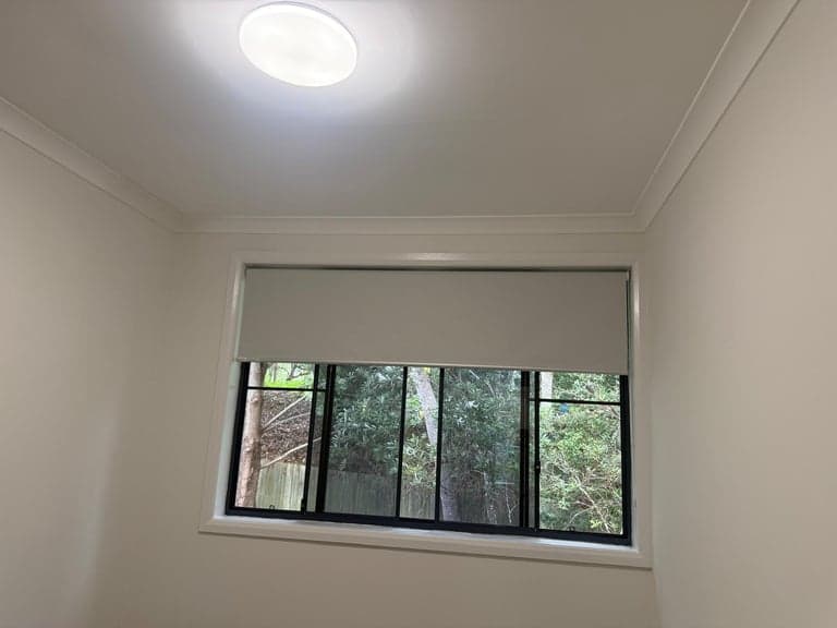 White roller blind fitted to a black-framed bedroom window in Sydney
