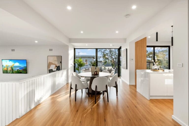 Warm oak flooring through an open Sydney dining room and white kitchen