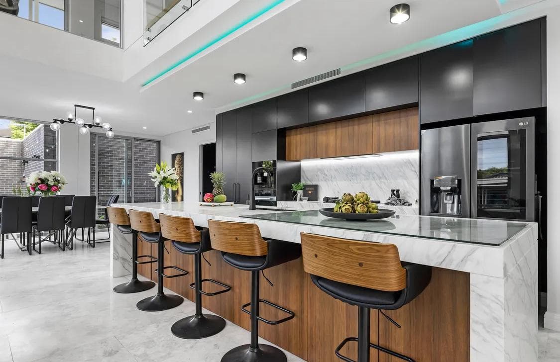 Marble island kitchen in Sydney with walnut joinery, black cabinets and timber stools