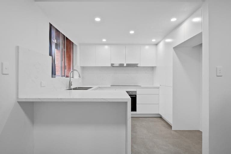 Compact handleless white kitchen in Sydney with a stone peninsula and hidden storage