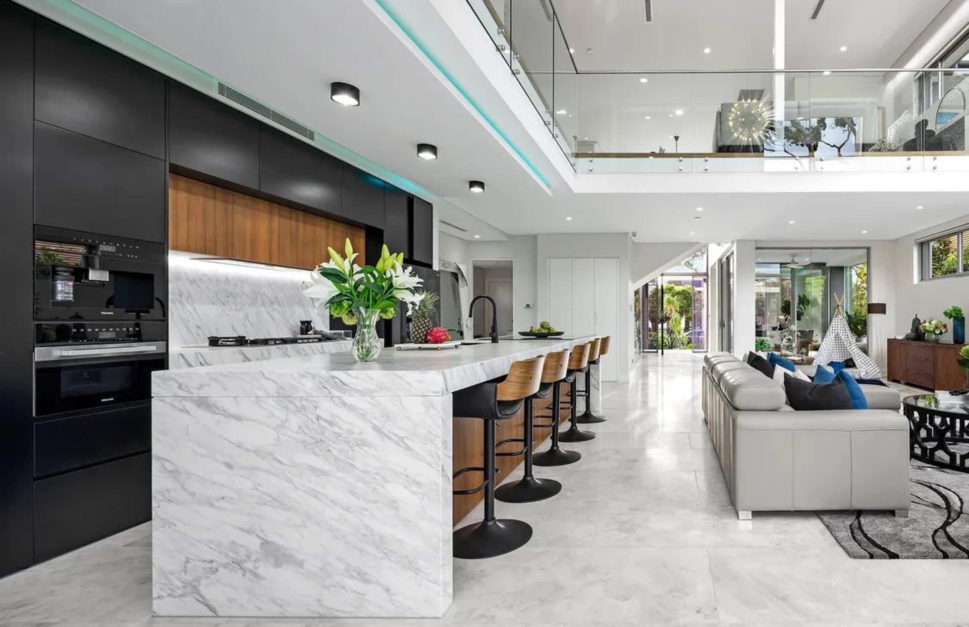 Open Sydney kitchen with a marble island, black cabinetry and timber stools