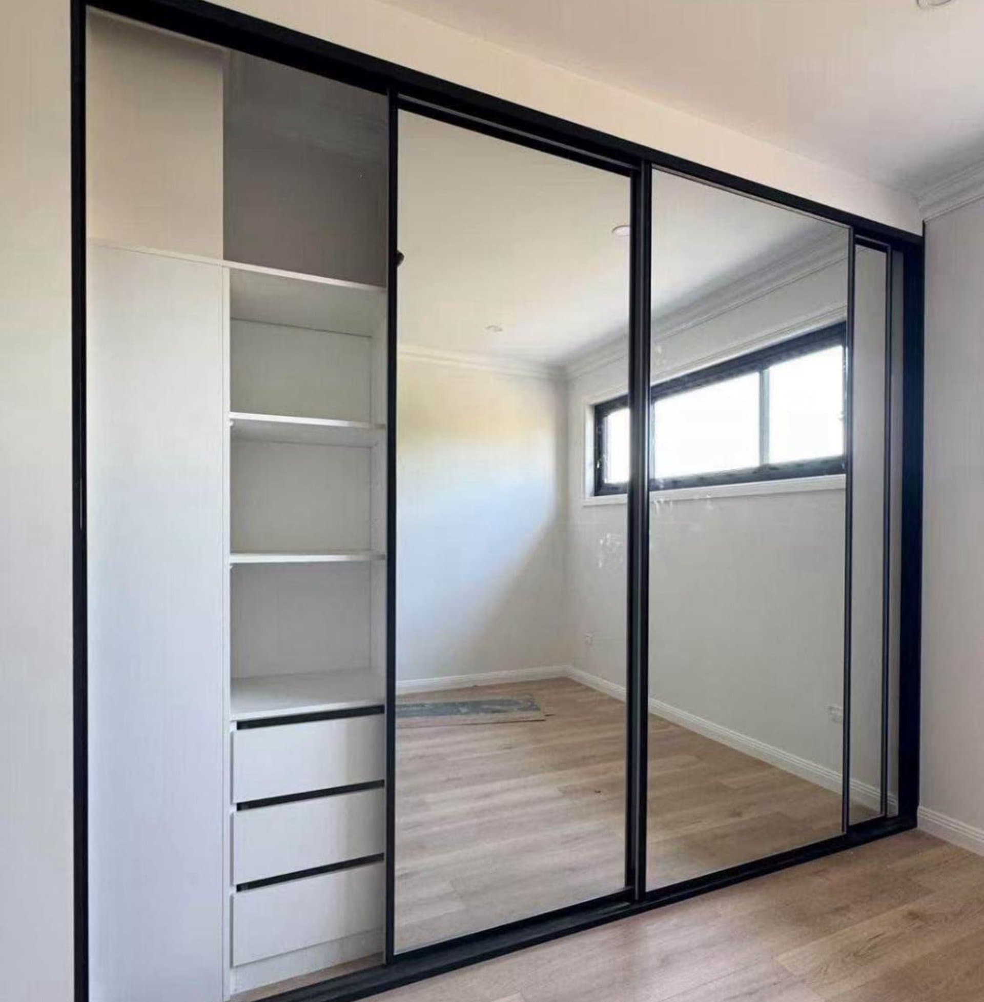 Black-framed mirrored sliding wardrobe with open white shelves in Sydney
